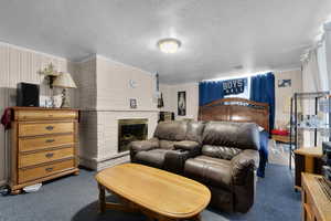 Carpeted bedroom with a brick fireplace, a textured ceiling, ornamental molding, and wood walls
