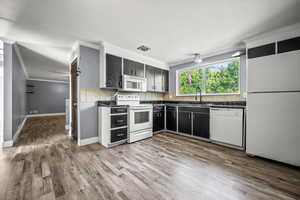 Kitchen featuring ornamental molding, dark countertops, white appliances, wood finished floors, and dark cabinets