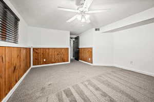 Spare room with a textured ceiling, carpet, wainscoting, ceiling fan, and wood walls