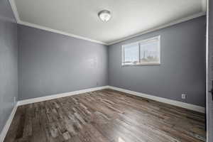 Empty room featuring ornamental molding and dark wood-style floors