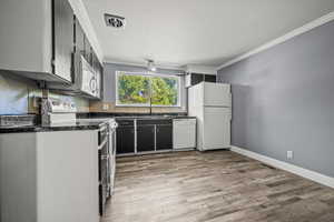 Kitchen featuring ornamental molding, white appliances, light wood-style flooring, dark stone counters, and dark cabinetry