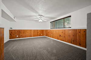 Carpeted empty room featuring a wainscoted wall, a ceiling fan, wood walls, and a textured ceiling
