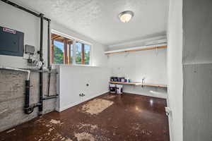 Laundry room with electric panel and a textured ceiling