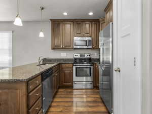 Kitchen featuring a peninsula, appliances with stainless steel finishes, dark wood-type flooring, recessed lighting, and dark stone counters