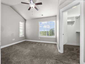 Unfurnished bedroom with dark colored carpet, a spacious closet, vaulted ceiling, and ceiling fan