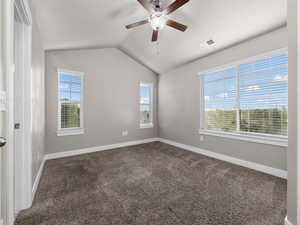 Unfurnished room featuring dark colored carpet, ceiling fan, and lofted ceiling