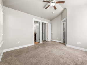 Unfurnished bedroom with carpet floors, vaulted ceiling, a walk in closet, ensuite bath, and a ceiling fan