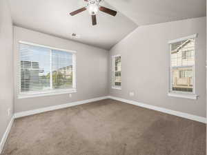 Unfurnished room featuring carpet, healthy amount of natural light, vaulted ceiling, and a ceiling fan