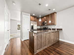 Kitchen featuring a peninsula, stainless steel appliances, dark stone counters, dark wood-type flooring, and a textured ceiling