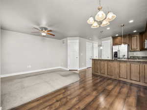 Kitchen featuring a ceiling fan, a chandelier, stainless steel fridge, dark wood-style floors, and stone counters