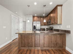 Kitchen with a peninsula, stainless steel appliances, dark stone countertops, dark wood-type flooring, and pendant lighting