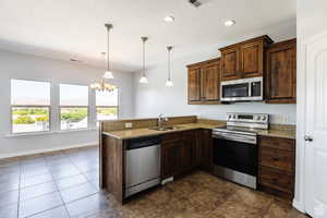 Kitchen with stainless steel appliances, a textured ceiling, a chandelier, light stone counters, and a peninsula