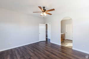 Empty room with dark wood-style flooring, arched walkways, and ceiling fan