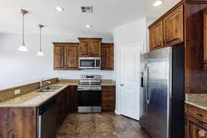 Kitchen featuring recessed lighting, stainless steel appliances, a textured ceiling, a peninsula, and light stone countertops