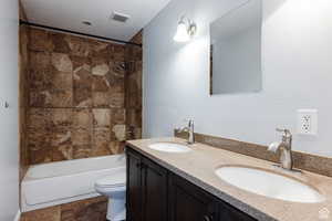 Bathroom featuring double vanity, tub / shower combination, and stone finish floors