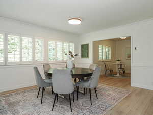 Dining room featuring ornamental molding, light wood-style flooring, and a wainscoted wall