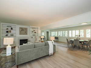 Living room with light wood-style flooring, a premium fireplace, crown molding, and built in shelves
