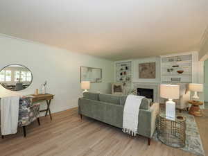 Living room featuring light wood finished floors, ornamental molding, a fireplace, and built in shelves