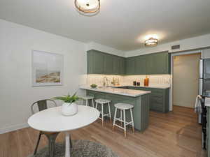 Kitchen featuring green cabinets, a peninsula, a kitchen bar, decorative backsplash, and light countertops