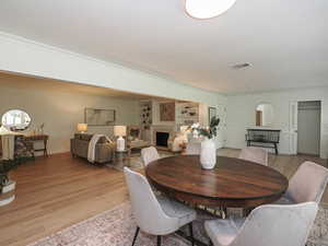 Dining room with light wood-style floors, ornamental molding, and a fireplace
