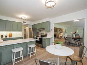 Kitchen featuring green cabinets, stainless steel appliances, light wood finished floors, and light countertops