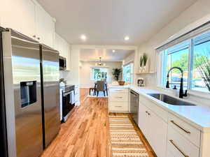 Kitchen featuring decorative backsplash, appliances with stainless steel finishes, white cabinetry, light wood-type flooring, and light countertops
