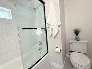 Full bath with combined bath / shower with glass door and tile patterned flooring