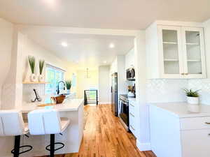 Kitchen with decorative backsplash, a breakfast bar, appliances with stainless steel finishes, white cabinets, and light countertops