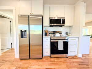 Kitchen featuring stainless steel appliances, light countertops, light wood finished floors, white cabinets, and tasteful backsplash