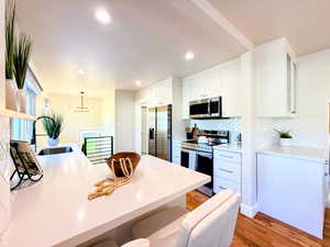 Kitchen featuring appliances with stainless steel finishes, a kitchen bar, light wood-style floors, light countertops, and recessed lighting