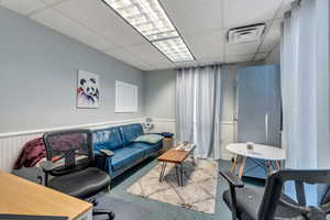 Living room featuring a drop ceiling, wainscoting, and carpet floors