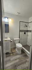 Bathroom with a textured ceiling, wood finished floors, vanity, and tiled shower