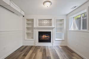 Unfurnished living room with a glass covered fireplace, wood finished floors, and built in shelves