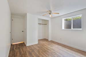 Unfurnished bedroom featuring a closet,  laminate wood finished floors, a textured ceiling, and a ceiling fan