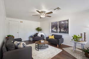 Living room with ceiling fan, dark wood-style floors, bright with natural light
