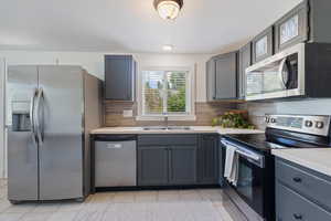 Kitchen featuring stainless steel appliances, light countertops, and gray cabinetry