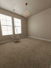 Empty room with a textured ceiling, a chandelier, and light colored carpet