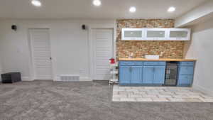 Indoor dry bar featuring light colored carpet, recessed lighting, and beverage cooler
