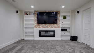 Unfurnished living room featuring carpet floors, built in features, and a glass covered fireplace