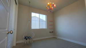 Carpeted spare room featuring baseboards and a chandelier
