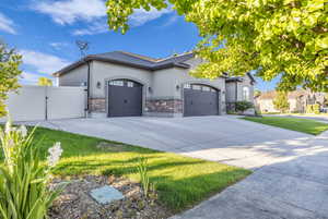 View of front facade featuring a garage, a gate, stucco siding, stone siding, and driveway