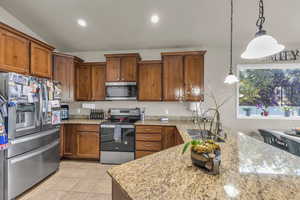 Kitchen with appliances with stainless steel finishes, recessed lighting, brown cabinets, pendant lighting, and light stone countertops