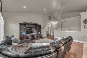 Living room with lofted ceiling, arched walkways, wood finished floors, and recessed lighting