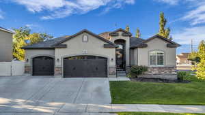 French provincial home featuring stone siding, stucco siding, a front yard, a garage, and concrete driveway