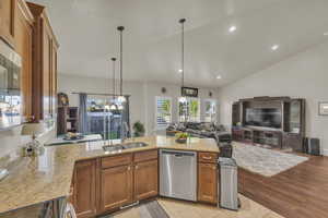 Kitchen featuring lofted ceiling, stainless steel dishwasher, brown cabinets, light stone counters, and electric range oven