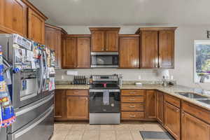Kitchen featuring stainless steel appliances, light stone counters, light tile patterned floors, and brown cabinetry