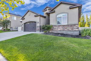 View of front facade with driveway, stucco siding, stone siding, and a front yard