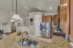 Kitchen featuring stainless steel fridge, light stone countertops, brown cabinetry, electric range, and recessed lighting