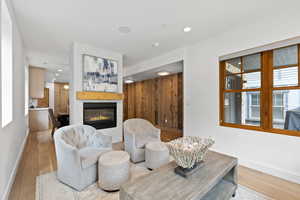Living area with light wood-type flooring, recessed lighting, a glass covered fireplace, and wooden walls