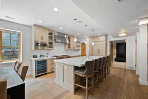 Kitchen with light wood-type flooring, light countertops, beverage cooler, recessed lighting, and a kitchen breakfast bar